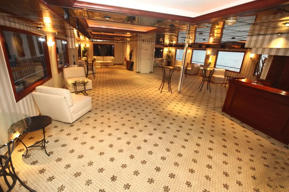 Window-lined lounge aboard the Cornucopia Destiny with white sofas and a wood bar